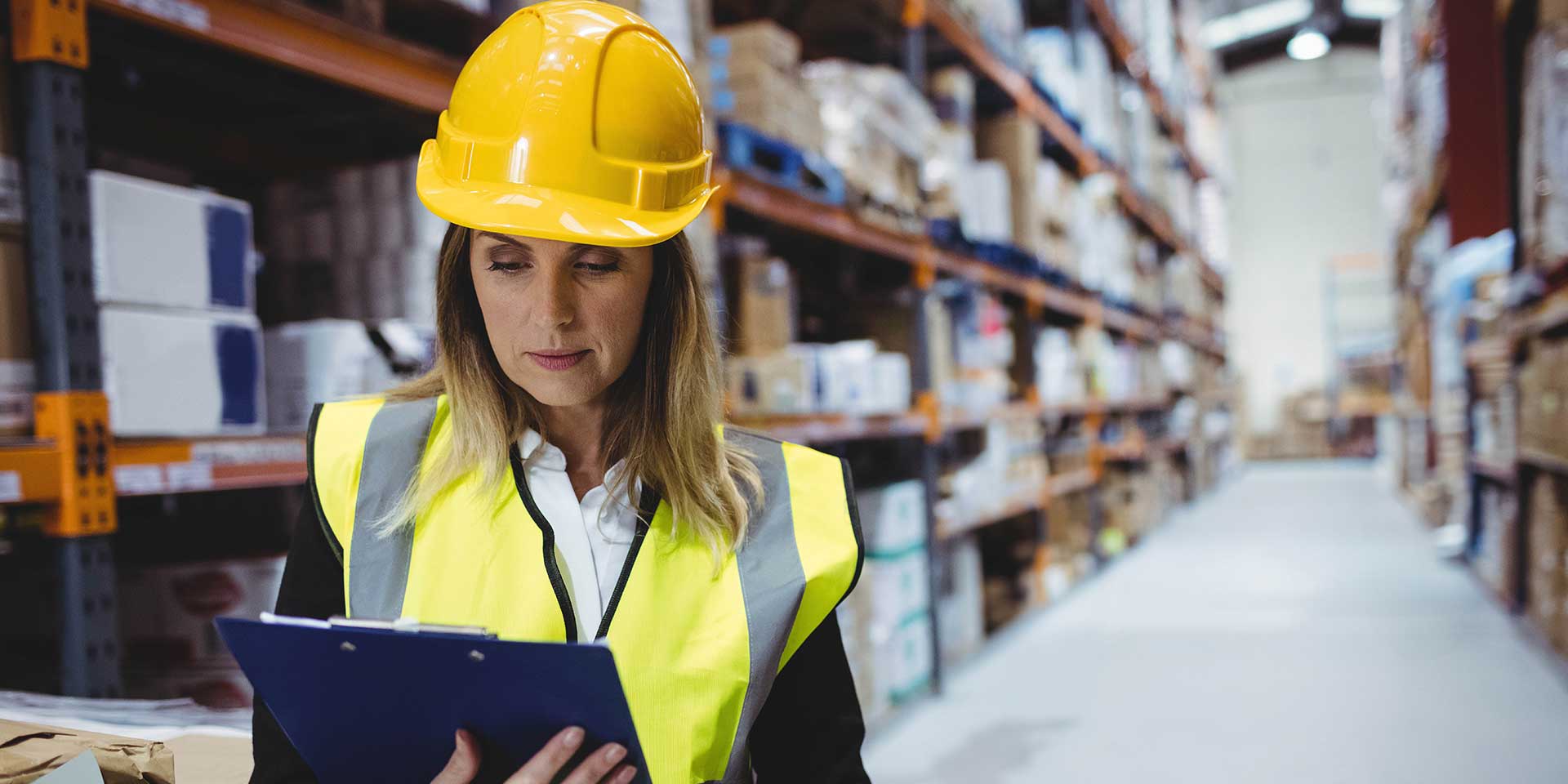 Frau in Sicherheitskleidung füllt im Lager Erfassungsbogen Arbeitsschutz.