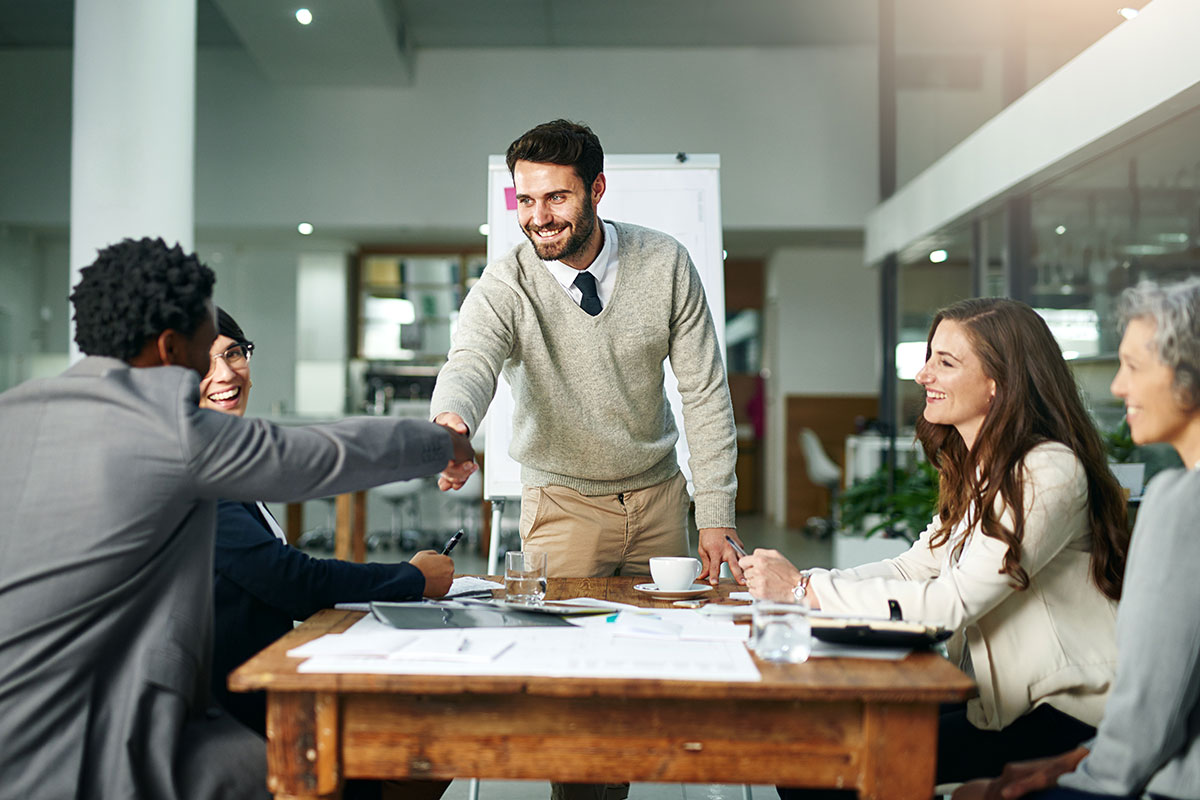 Unternehmer begrüßt potenzielle Investoren bei einem Meeting und schüttelt einem von ihnen die Hand.