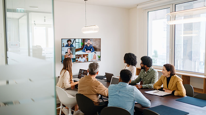 Team im Besprechungsraum nimmt an einem Video-Meeting mit Kolleg*innen im Homeoffice teil.