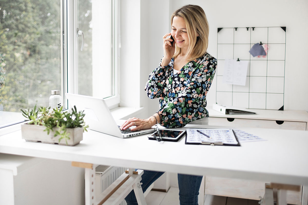 Eine Mitarbeiterin steht an ihrem höhenverstellbarem Schreibtisch und telefoniert.