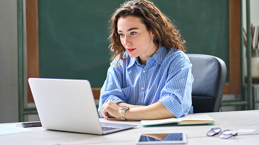 Frau arbeitet konzentriert am Laptop im Büro und nimmt an einem virtuellen Meeting teil.