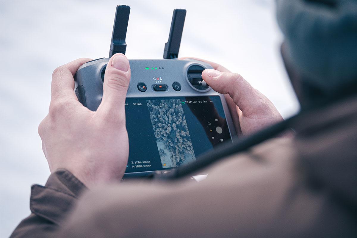 Hände bedienen eine Drohnensteuerung mit Display zur Live-Übertragung während des Flugs.