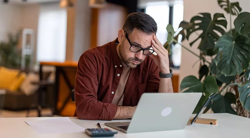 Mann arbeitet am Laptop und ist verzweifelt aufgrund fehlender Informationssicherheit.