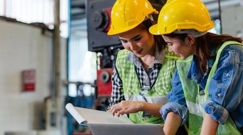 Zwei Ingenieurinnen oder Technikerinnen mit Schutzhelm besprechen ein Projekt in einer Industriefabrik. © Adobe Stock, winnievinzence