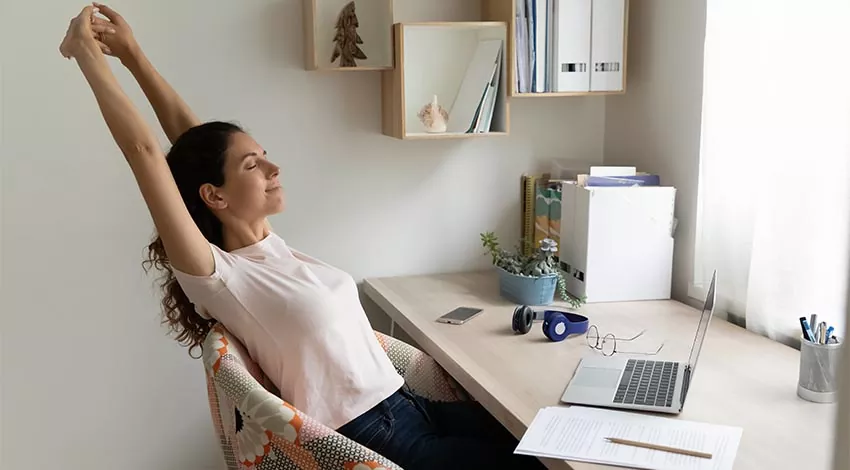 Frau im Home Office macht eine kurze Pause und streckt sich auf ihrem Stuhl © Adobe Stock, fizkes