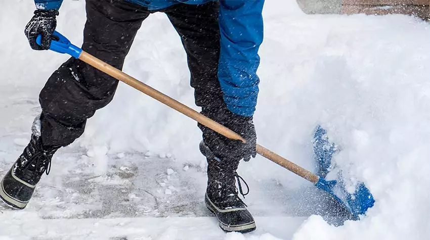 Mitarbeiter führt den Winterdienst, indem er mit einer Schaufel das Betriebsgelände von Schnee befreit. © Adobe Stock, chiyacat