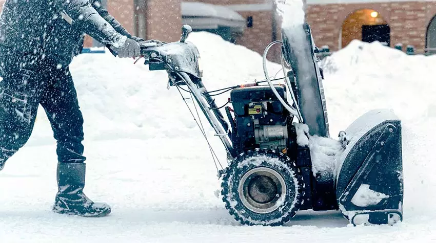 Mitarbeiter nutzt für den Winterdienst eine Schneefräse. Mitarbeiter führt den Winterdienst, indem er mit einer Schaufel das Betriebsgelände von Schnee befreit. © Adobe Stock, I