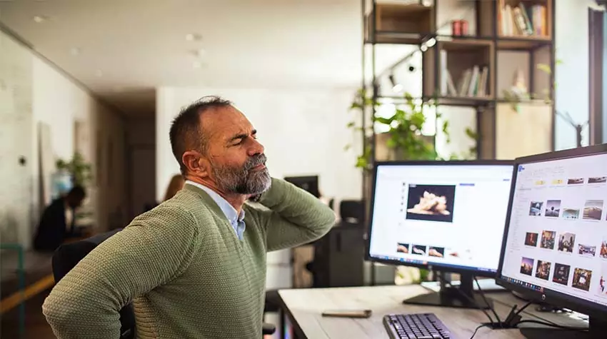 Mitarbeiter sitzt mit Rückenschmerzen am Schreibtisch in einem Green Office. © Adobe Stock, Geber86